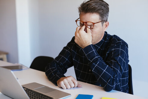 Geschäftsmann am Schreibtisch im Büro und reibt sich die Augen - EBSF02091