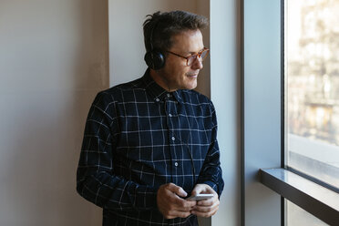Geschäftsmann mit Kopfhörern und Mobiltelefon schaut aus dem Fenster - EBSF02092