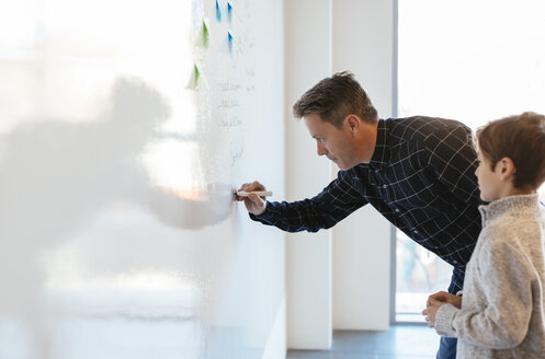 Geschäftsmann im Büro schreibt auf Whiteboard mit Sohn beobachtet ihn - EBSF02100