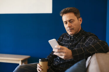 Businessman with takeaway coffee sitting and looking on cell phone - EBSF02101