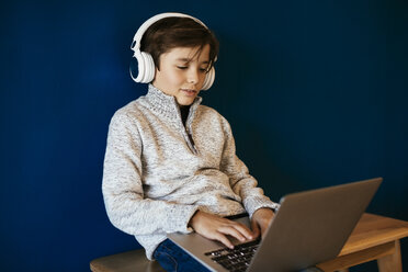 Boy sitting on bench wearing headphones and using laptop - EBSF02105