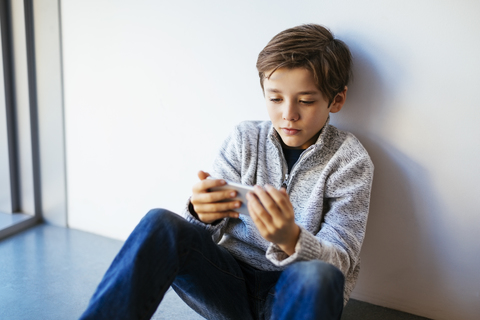 Boy sitting on floor looking at cell phone stock photo