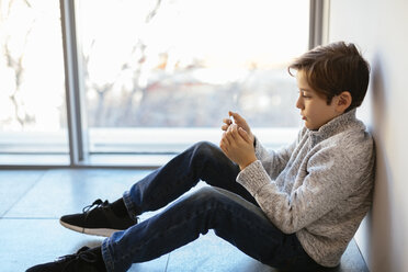 Junge sitzt auf dem Boden und schaut auf sein Handy - EBSF02111