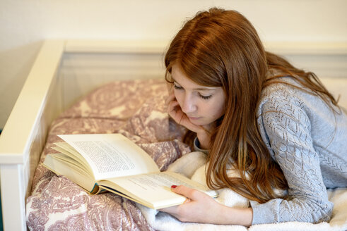 Rothaariges Teenager-Mädchen liegt auf dem Bett und liest ein Buch - LBF01759