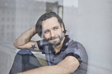 Portrait of smiling man sitting behind windowpane - PNEF00511