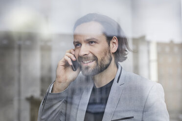 Porträt eines lächelnden Geschäftsmannes am Telefon hinter einer Fensterscheibe - PNEF00514