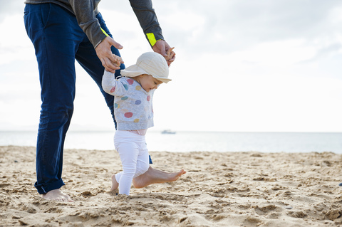 Spanien, Lanzarote, kleines Mädchen, das mit Hilfe seines Vaters am Strand spazieren geht, lizenzfreies Stockfoto