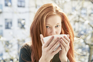 Portrait of redheaded woman drinking bowl of white coffee on balcony - FMKF04764