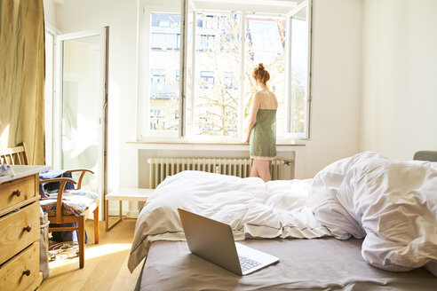 Rückenansicht einer Frau im Schlafzimmer mit Blick aus dem Fenster - FMKF04770