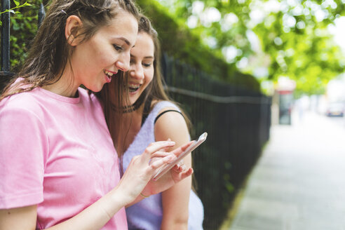 Zwei glückliche Teenager-Mädchen mit Handy im Freien - WPEF00004