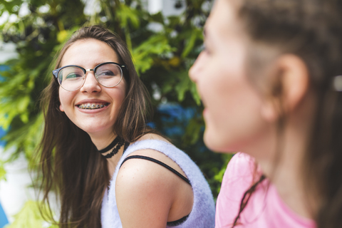 Glückliches Teenager-Mädchen mit Zahnspange und Brille, das einen Freund ansieht, lizenzfreies Stockfoto