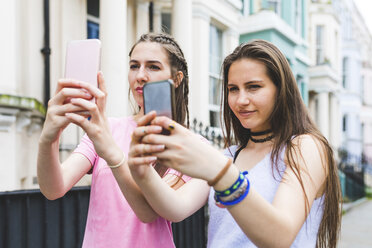 Zwei Mädchen im Teenageralter in der Stadt, die nebeneinander stehen und Selfies machen - WPEF00010