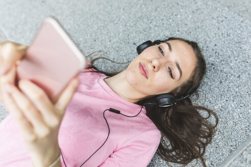 Entspannte junge Frau im Liegen mit Handy und Kopfhörern - WPEF00024
