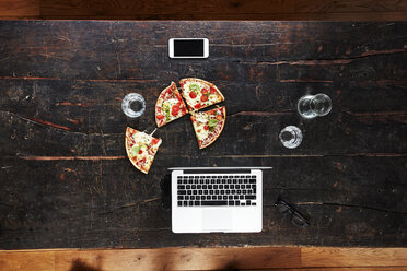 Laptop, smartphone, pizza and water glasses on tabletop, top view - FMKF04787