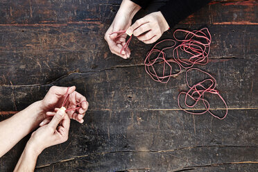 Hands of man and woman playing with rubber bands, top view - FMKF04790