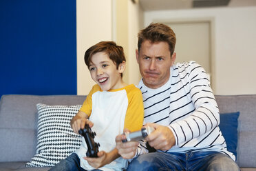 Father and son playing video game on couch at home - EBSF02113