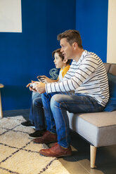 Vater und Sohn spielen ein Videospiel auf der Couch zu Hause - EBSF02114