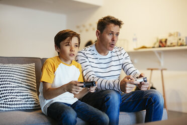 Vater und Sohn spielen ein Videospiel auf der Couch zu Hause - EBSF02115