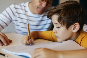 Father watching son doing homework at table - EBSF02120