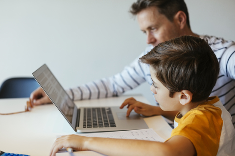 Vater und Sohn an einem Tisch mit einem Jungen, der einen Laptop benutzt, lizenzfreies Stockfoto