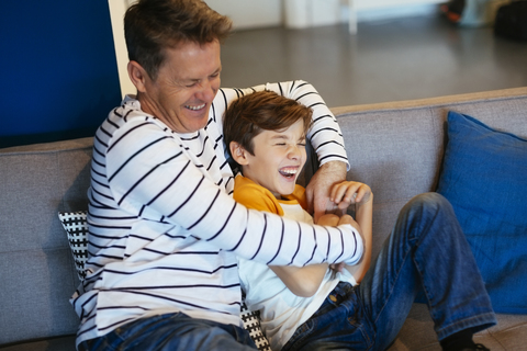 Carefree father and son having fun on couch at home stock photo