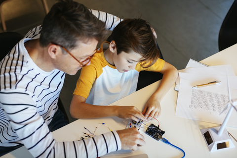 Father and son assembling a construction kit with wind turbine model stock photo