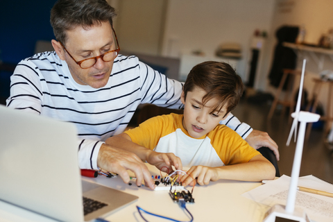 Vater und Sohn beim Zusammenbau eines Baukastens mit Laptop und Windradmodell, lizenzfreies Stockfoto