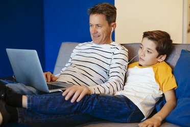 Father and son with earbuds and laptop on couch at home - EBSF02140