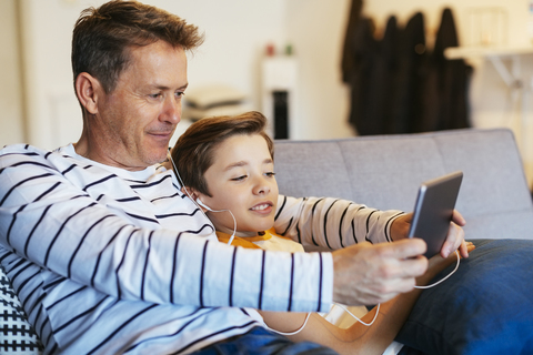 Father and son with earbuds and tablet on couch at home stock photo