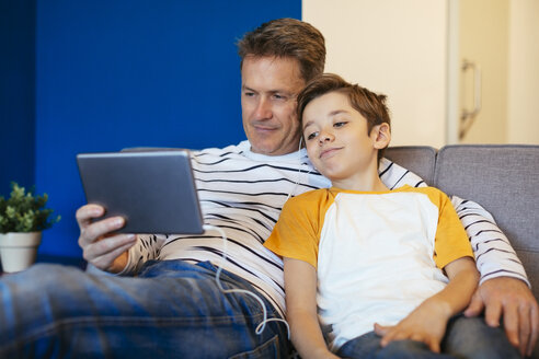 Vater und Sohn mit Ohrstöpseln und Tablet auf der Couch zu Hause - EBSF02143