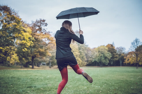 Rückenansicht einer jungen Frau mit Regenschirm, die in einem herbstlichen Park tanzt - JSCF00028