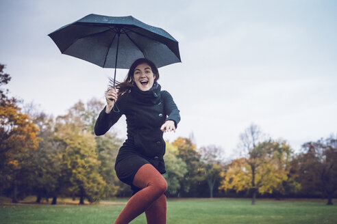 Porträt einer glücklichen jungen Frau mit Regenschirm, die in einem herbstlichen Park tanzt - JSCF00030