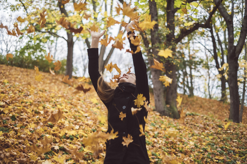 Glückliche junge Frau wirft Herbstblätter in die Luft, lizenzfreies Stockfoto