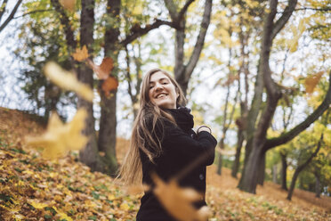 Porträt einer glücklichen jungen Frau, die Herbstblätter in die Luft wirft - JSCF00040