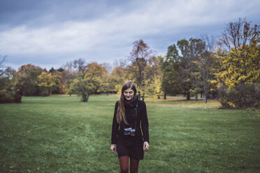 Young woman with camera walking on a meadow in autumnal park - JSCF00048