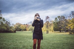 Junge Frau fotografiert mit Kamera auf einer Wiese im herbstlichen Park - JSCF00050