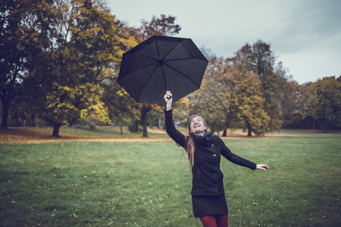 Junge Frau tanzt mit Regenschirm im herbstlichen Park, lizenzfreies Stockfoto
