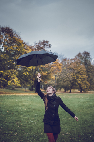 Glückliche junge Frau tanzt mit Regenschirm im herbstlichen Park, lizenzfreies Stockfoto