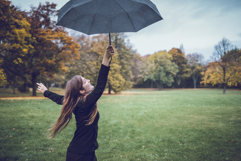 Glückliche junge Frau tanzt mit Regenschirm im herbstlichen Park, lizenzfreies Stockfoto
