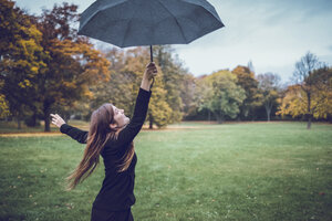 Glückliche junge Frau tanzt mit Regenschirm im herbstlichen Park - JSCF00053