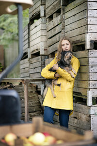 Frau auf einem Bauernhof steht an Holzkisten und hält einen Hund - PESF00958