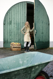 Lächelnde Frau auf einem Bauernhof, die an einer Kiste mit Äpfeln steht - PESF00968