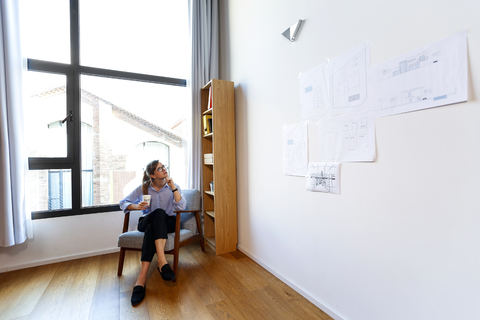 Junger Architekt sitzt im Büro und schaut auf die Pinnwand, lizenzfreies Stockfoto