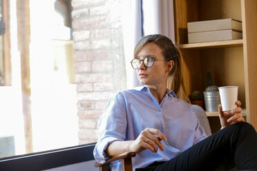 Young woman with coffee cup looking out of office window - VABF01468