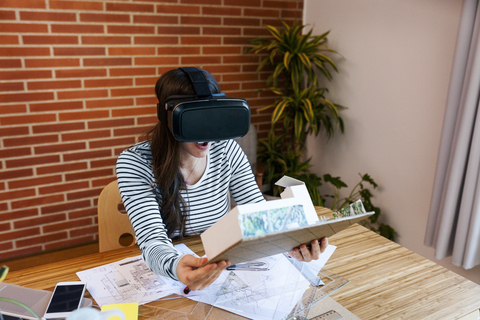 Junge Frau arbeitet in einem Architekturbüro und betrachtet ein Modell mit einer VR-Brille, lizenzfreies Stockfoto