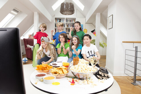 Group of kids watching soccer world championship with table full of sweets and snacks - NEKF00017