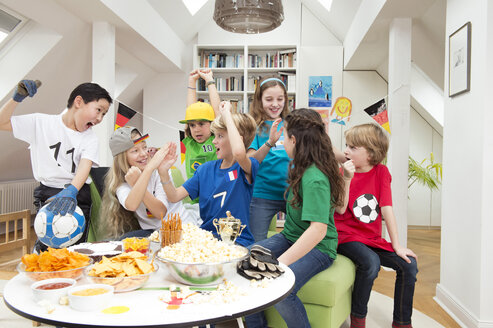 Gruppe von Kindern, die sich die Fußballweltmeisterschaft mit einem Tisch voller Süßigkeiten und Snacks ansehen - NEKF00018