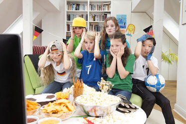 Gruppe von Kindern, die sich die Fußballweltmeisterschaft mit einem Tisch voller Süßigkeiten und Snacks ansehen - NEKF00019