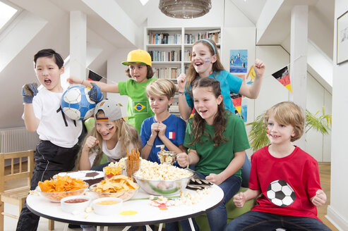 Gruppe von Kindern, die sich die Fußballweltmeisterschaft mit einem Tisch voller Süßigkeiten und Snacks ansehen - NEKF00020