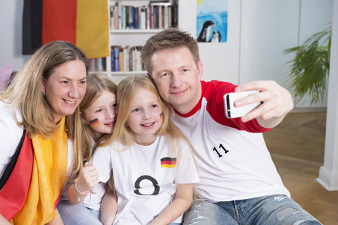 Familie schaut Fußballweltmeisterschaft und macht ein Smartphone-Selfie, lizenzfreies Stockfoto